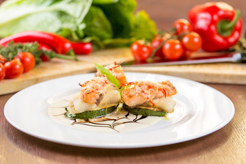 Fried zucchini with slices of fish. On a white plate and wooden table