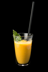 Mango smoothie in a glass with a straw. On a black background