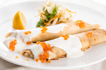 Pancakes with caviar and sour cream. On a white plate