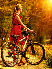 Obraz premium Girl with bicycle. Girl wearing sundress rides bicycle into park have rest. Girl in autumn park. Bicycle girl look away. Back view.