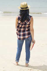 young woman standing on the beach with book in hand