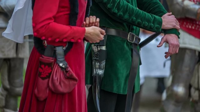 A prince and princess are standing outside in the courtyard and a princess is talking. A young man is watching her and smiling. Close-up shot.
