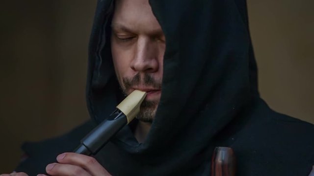 A man who is dressed in a hoodie is playing a flute and he is putting all his emotions inside. Close-up shot.
