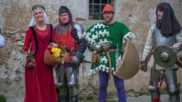 Princess is holding a basket with red and yellow roses and she is giving them to the knights that are going to fight in a battle. Wide-angle shot.
