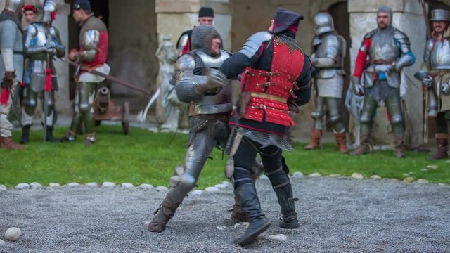 Two knights are fencing with each other and then one of them is stronger than the other and the weaker one falls on the ground and is killed. Wide-angle shot.
