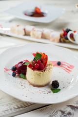 Small cake with mint leaf. Blackberry and currant. Appetizing cheesecake on a plate. Sweet taste of art.