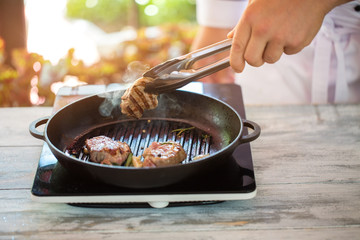 Tongs hold piece of meat. Man's hand near frying pan. Juicy roasted beef. How to cook savoury breakfast.
