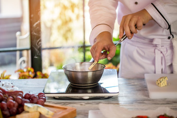 Slice of cheese on knife. Small cooker and saucepan. French cheese for sauce. It's the last ingredient.