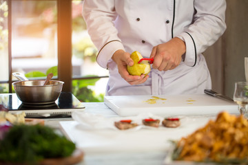 Man's hand peeling a pear. Chef near white cooking board. Sweet ingredient for sauce. Need fresh fruit.