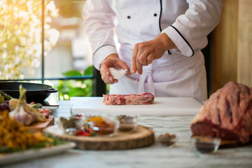 Obraz na płótnie Canvas Hand holds bowl with salt. Tendeloin on cooking board. Spice needed for taste. Chef of restaurant prepares steak.
