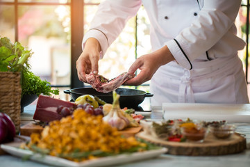Hands hold piece of meat. Frying pan near cooking board. Beef spiced with pepper. Process of preparing steak.