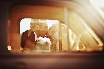 Warm picture of newlyweds kissing behind an old car