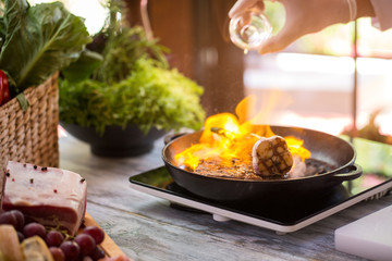 Flame in frying pan. Hand holds bottle over pan. Skilled chef makes a steak. Preparation of beef.