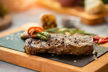 Piece of brown meat. Steak on a board. Beef spiced with black pepper. Appetizing lunch in local restaurant.