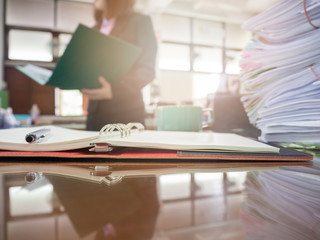 Pile of unfinished documents on office desk with businesswoman background