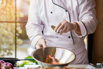 Raw meat in a bowl. Chef's hand holds bay leaf. Add spice to pork. Cook busy in the kitchen.