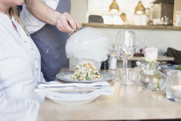 Midsection of waiter lifting cloche from dish for customer in restaurant