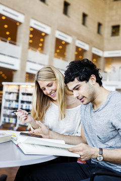 Happy young friends with mobile phone reading notes in library