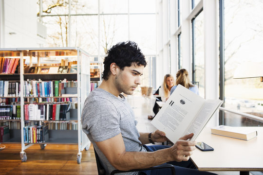 Young man reading book at table in library