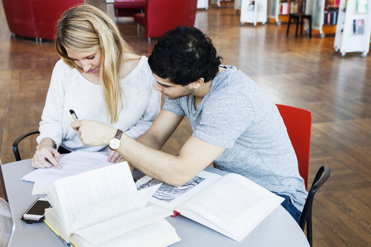 High angle view of multiethnic friends discussing over notes at table in library