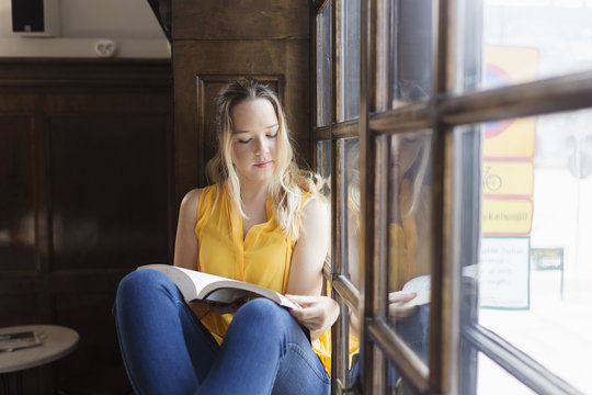 Young woman sitting by window, reading book