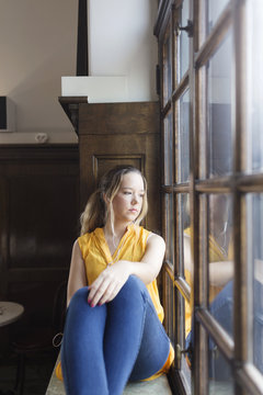 Young pensive woman sitting by window