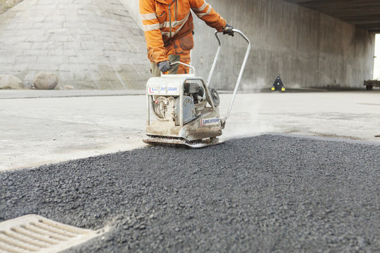 Low section of manual worker laying asphalt at road construction site