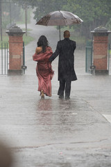 Indian smartly dressed couple holding an umbrella in the rain.