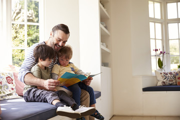 Father And Sons Reading Story At Home Together