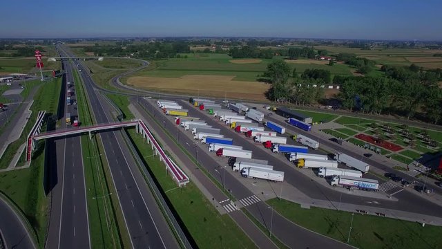 Fly over parking lot for truck lorries both sides of highway road with pedestrian overpass bridge above and gas filling station aerial top view 4K HD. Drivers working hours truck stop and rest area