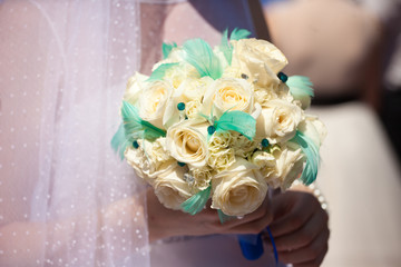 Bride holds reach wedding bouquet decorated with feathers and cr