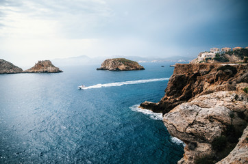 Fototapeta na wymiar The yacht sails near the rocks of Santa Ponsa in the mediterranean sea before the storm, Mallorca Island