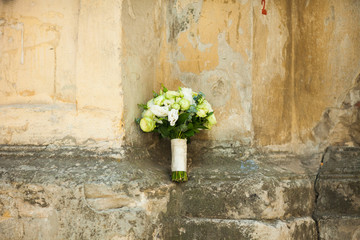 Green wedding bouquet lies on the old stone building