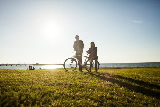 Couple with bicycle on grassy landscape by sea against sky