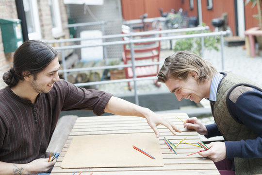 Happy male friends playing Mikado at cafe backyard