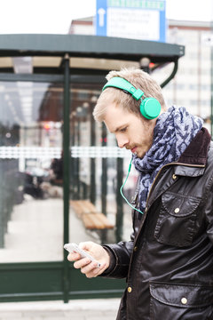 Side view of man listening music through mobile phone while waiting at bus stop