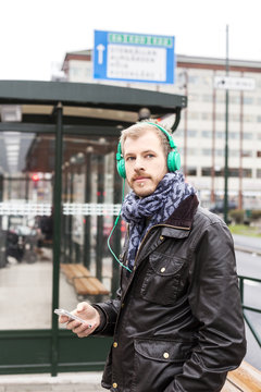 Man listening music through mobile phone while waiting at bus stop