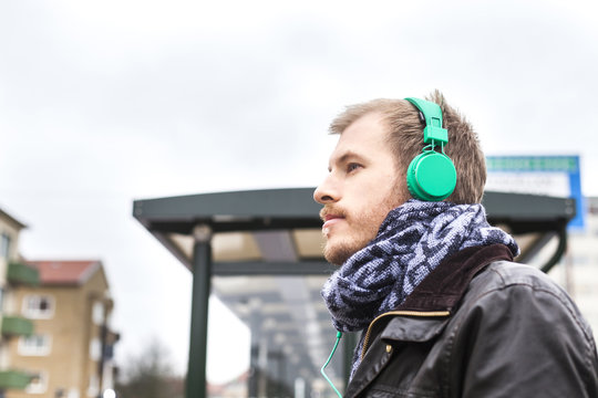 Side view of man listening music at bus stop against clear sky