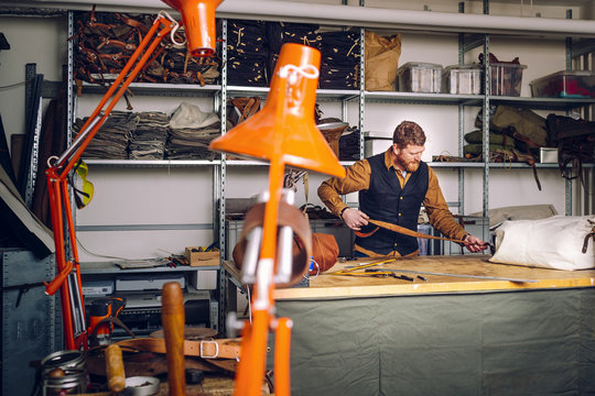 Male worker attaching leather belt to bag at worktable in factory