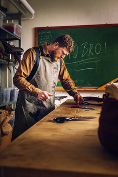 Male worker holding ruler while manufacturing bag at worktable in factory