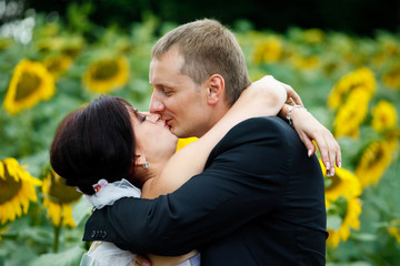 Fototapeta premium Bride holds her hands on groom's neck while he kisses her behind