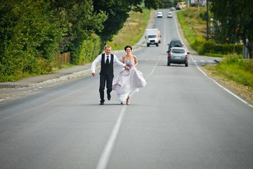 Happy wedding couple runs across the highway