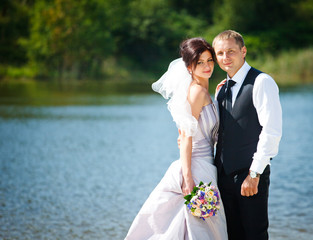 Groom hugs bride delicately standing in the front of a lake