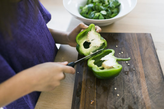 Cropped image of girl slicing bell pepper on cutting board in kitchen