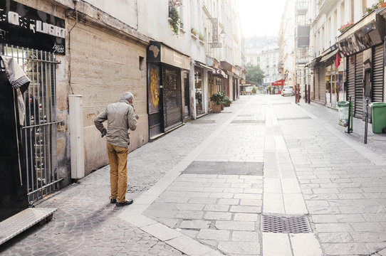 Rear view of senior man standing on sidewalk amidst buildings
