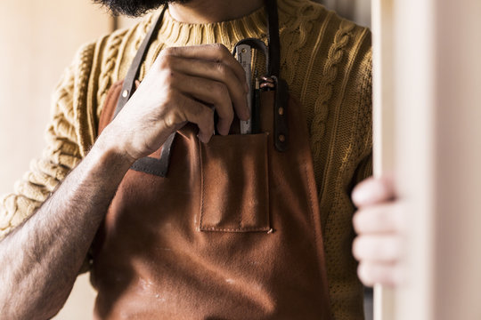 Midsection of carpenter keeping ruler in apron pocket at workshop