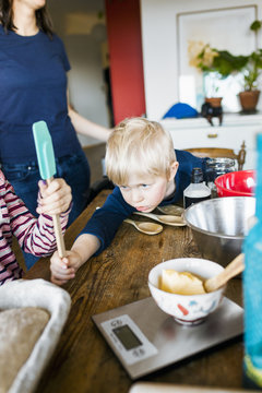 Little boy with sister holding scraper while mother standing at table