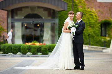 Smiling bride leans to a groom standing in the front of hotel en