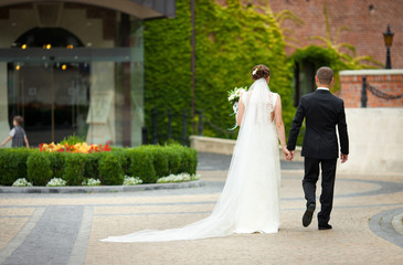 Bride and groom in black suit walk around the flower-bed