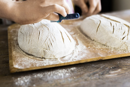Baker's hands making design on dough at table in bakery